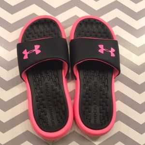 A pair of pink and black under armour slides.